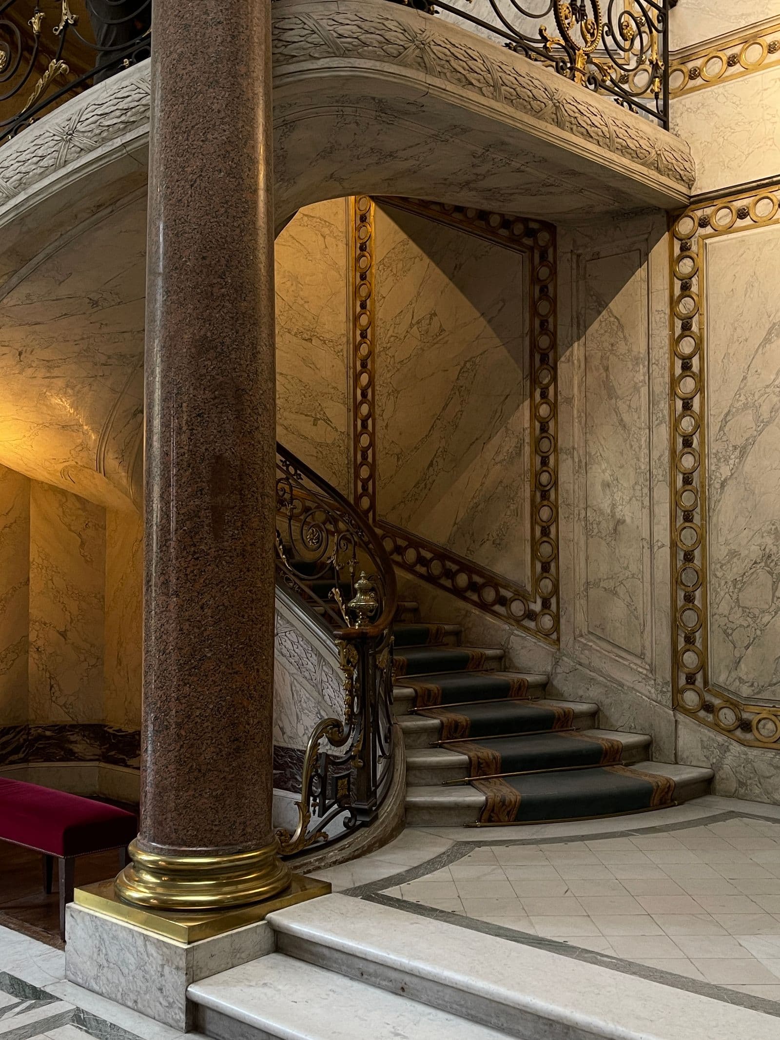 Cage d'escalier d'un immeuble ancien : escalier en colimaçon à marches de pierre et de marbre, rampe ouvragée et colonne.