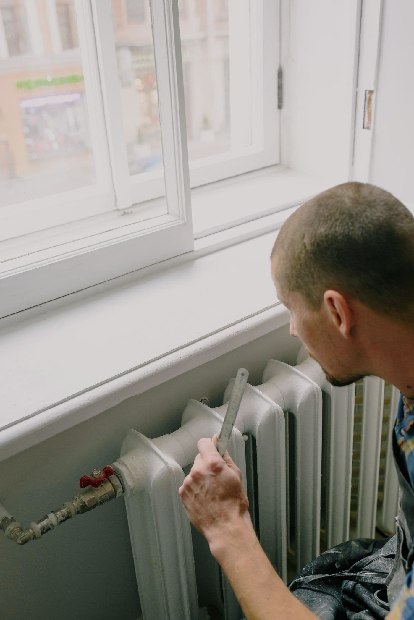 Installateur intervenant sur un radiateur sous une fenêtre, en pose de chauffage dans un logement en rénovation.