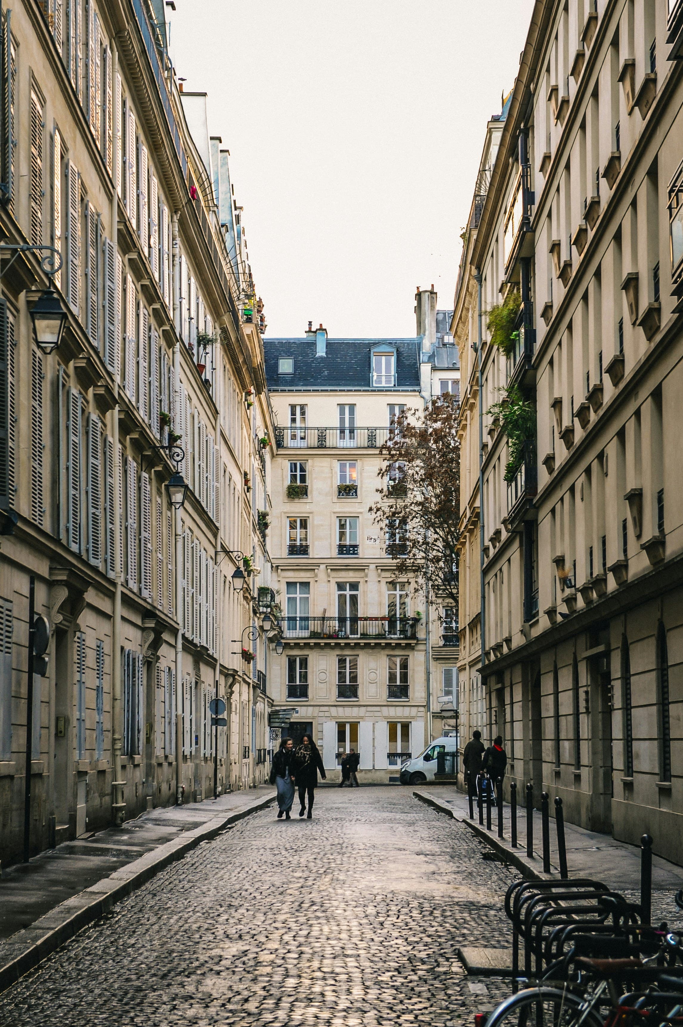 Rue parisienne pavée bordée d'immeubles haussmanniens en pierre calcaire, garde-corps et balcons en fer forgé.