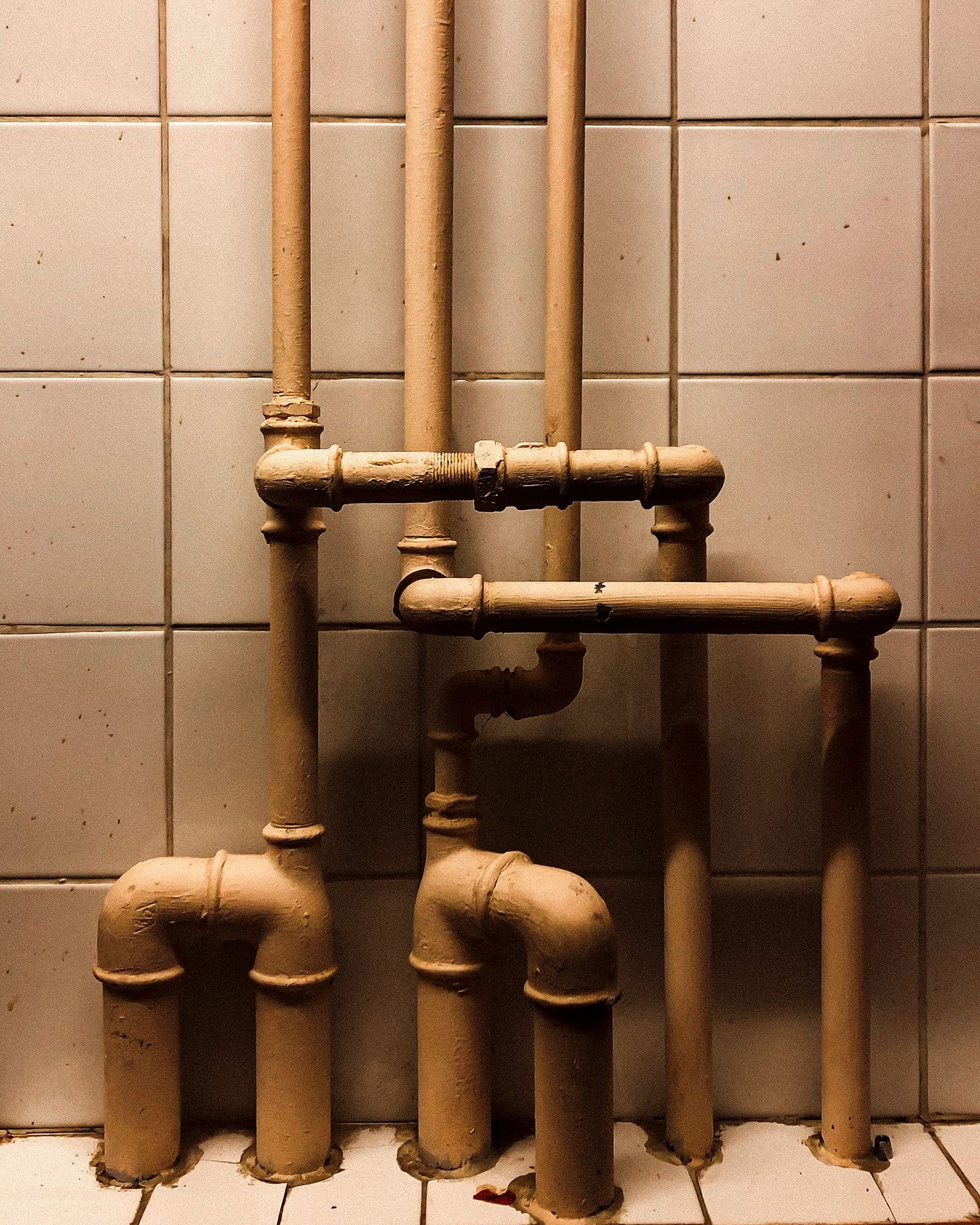 Canalisations de plomberie en laiton et cuivre le long d'un mur carrelé, coudes et raccords — installation technique d'immeuble.
