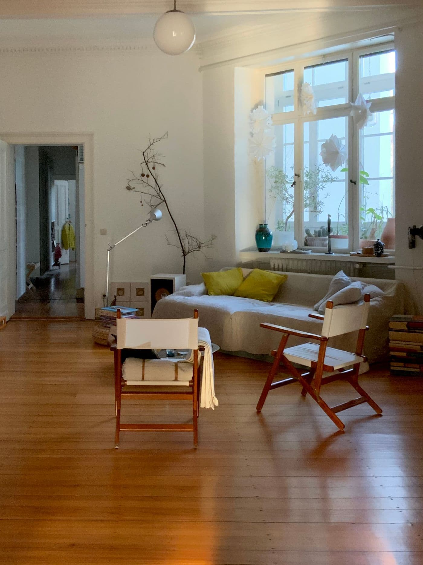 Séjour de maison rénovée : salon lumineux aux tons chauds, fauteuils en bois, plantes et grandes fenêtres.